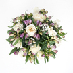 This sympathy bouquet is captured from above, perfectly centred on a clean white background that allows its gentle colours and textures to breathe. At its core are several creamy white roses, their petals arranged in delicate spirals that shift subtly from snow white at the outer edges to warm ivory and a hint of peach deeper within. Some of the roses are fully open, revealing every fold and curve, while others remain partly enclosed, adding depth and a sense of unfolding time. Nestled between them are slender stems of purple alstroemeria, most still in bud, their long, tapered shapes exhibiting a quiet gradient from fresh, leafy green at the base to muted lavender, lilac, and soft plum at the tips. A few buds have just begun to crack open, hinting at fine internal stripes and the more vivid petals to come. Sprinkled throughout are airy tufts of white baby's breath, each tiny flower a soft dot of light that gives the bouquet an almost cloud-like halo. Surrounding everything is a generous collar of deep green foliage, smooth and slightly glossy, which shapes the bouquet into a compact, spherical form and adds a reassuring richness to the palette. The lighting is gentle and even, with no harsh shadows, as though the flowers were laid on a quiet table in a North Watford living room after the family returned from a service. Balanced and composed, this arrangement feels like a tender embrace in floral form, crafted to bring a measure of calm and consolation when words are difficult.