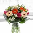 Overflowing with colour and expertly designed by a North Watford florist, this bouquet features an enchanting blend of textures and tones. The arrangement's focal points-bold orange gerbera daisies and their softer peach counterparts-glow with cheerful vitality, like a burst of sunshine along North Watford's leafy lanes. Nestled between them, deep magenta roses impart a romantic richness, their velvety spirals drawing the eye and inviting admiration. Gathering in gentle support, clusters of pristine white alstroemeria and small spray roses offer moments of brightness and purity, reminiscent of a fresh morning in Watford Fields. Slender touches of blush pink and dainty white fillers peek through, building a sense of depth and intricate beauty. Broad, paddle-like green leaves wrap gracefully around the base, anchoring the bouquet with a protective, organic collar, while finer greenery adds texture and movement throughout. Presented in a tall, slender glass vase, the vibrant stems remain visible-a nod to freshness and transparency. The whole composition is bathed in soft, diffused daylight, ensuring that every colour and detail feels vivid and full of life. Ideal for celebrating special moments or expressing heartfelt gratitude to someone in North Watford, this bouquet exudes joy, care, and the artistic expertise of florists dedicated to their community.
