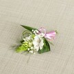 A delicately handcrafted boutonniere lies on a softly textured, light beige linen-style fabric, the neutral background allowing every petal and leaf to stand out in gentle detail. At the heart of the design is a single white alstroemeria bloom, its broad, velvety petals opening fully to reveal fine reddish-brown speckles and graceful stamens clustered at the throat. Just to the left, a vivid lime-green conical spike of tightly packed buds, reminiscent of Ornithogalum, adds sculptural interest and a touch of modern flair, its scale-like texture creating a striking contrast against the smooth lily petals. Around these focal elements, clouds of dainty white baby's breath float like tiny stars, softening the outline of the piece and giving it a light, romantic air that feels perfect for a wedding, prom, or formal celebration in North Watford. The greenery is carefully balanced: broad, deep green leaves form a sturdy base, while finer, grass-like fronds arc delicately from beneath the flowers, lending movement and a sense of natural spontaneity, as though freshly gathered from a garden near Cassiobury Park. At the right edge, the stems are neatly bound and finished with a glossy pink satin ribbon, tied into a small, perfectly shaped bow that lends a playful pop of colour and a hint of sweetness. The lighting is even and soft, with no harsh shadows, highlighting the freshness of the flowers and the careful craftsmanship of the arrangement, making it easy to picture this boutonniere pinned to a lapel on a bright North Watford wedding morning.