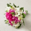 Nestled upon a pale, soft-textured fabric beside the bustling streets of North Watford, a joyous hand-tied bouquet radiates both elegance and exuberance. Dominating the composition are large, fuchsia-pink peonies, their lush, ruffled petals layered thickly to create a sense of abundant vitality and celebration. Intermixed with these are bright white Alstroemeria-their dainty, star-shaped petals marked with slender maroon pinstripes-bringing lightness and intricate beauty to the arrangement. Here and there, spikes of fresh, vivid green buds, likely Veronica or emerging hyacinth florets, reach upward, introducing lively energy reminiscent of the fresh growth seen in the community's nearby gardens this season. Creamy bell-shaped filler flowers provide a gentle softness that balances the bold hues, while broad, dark green leaves weave throughout for depth. The stems, expertly wrapped in a shining fuchsia satin ribbon, reflect the skill and attention to detail characteristic of North Watford's finest florists. This bouquet, perfect as a bride's companion or the focal point for a joyful occasion, seems to capture the very spirit of celebration and new beginnings so often marked in the area's gathering halls and local events. Every petal, every flourish invites the senses to experience not just colour, but the warmth of local tradition and the artistry behind every arrangement.
