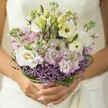 The essence of a North Watford spring wedding is crystallized in this close-up photo-an ethereal bridal bouquet held in gentle hands, suffused with pastel serenity. Creamy lisianthus blooms, their petals curling in soft ruffles, are enveloped by clusters of fragrant stock in pale pink and lavender shades, reminding one of early morning walks through Oxhey Park. A crown of vibrant purple allium, with its stars radiating from the bouquet's base, brings contrast and whimsical allure, gently anchoring the arrangement. Woven loops of glossy green bear grass ripple above, adding modern flair and subtle structure, like gentle echoes of the River Colne's banks. Manicured hands, nails painted blush, cradle the stems; the folds of an ivory gown hover in the background, offering just a whisper of texture and light. This bouquet, perfect for a Watford bride cherishing romance and hope, suggests purity and joy. Each bloom seems to emit a delicate fragrance, binding the senses in anticipation of a radiant North Watford celebration-a testament to the heart and expertise of the area's florists, ready to deliver beauty and happiness on the most important of days.