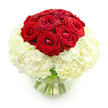A sophisticated floral arrangement of red roses and white hydrangeas is displayed in a rounded, transparent glass vase, set against a crisp white background that accentuates every curve and petal. At the top, approximately ten red roses are gathered tightly into a domed cluster, their velvety petals layered in rich, crimson spirals that convey warmth, intensity, and lasting affection. Some blooms are fully open, revealing their intricate centers, while others are still slightly cupped, adding depth and natural variation to the design. Encircling this central rose cluster is a generous collar of white hydrangeas, or similarly soft white blooms, densely packed into a full, cloud-like base. The countless tiny petals of the hydrangea create a plush, textured surface that feels comforting, almost like fabric, and their soft, creamy white hue makes the red roses stand out vividly. The clear glass vase, shaped like a gentle bubble, is half-filled with water, allowing a glimpse of the straight, green stems gathered together with deliberate care. Light reflects off the glass and water, giving the arrangement a clean, contemporary edge while still feeling romantic and classic. It is easy to imagine this bouquet gracing a dining table in a North Watford home near Woodside or adorning a quiet corner of a local restaurant during an anniversary celebration. The overall impression is of a carefully composed, heartfelt gift-something chosen to express deep love, appreciation, and the desire to make a special moment feel truly memorable.