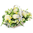 A light-toned wicker basket brimming with pastel funeral flowers is set against a crisp white background, giving the whole arrangement an air of calm and refinement that suits a North Watford memorial. The basket is gently oval with a tall, matching handle rising over the centre, its pale beige or off-white weave adding a natural softness. Inside, the flowers form a full, rounded dome, with no empty spaces, as if carefully shaped by an experienced local florist. At the forefront, large creamy white roses open in luxurious spirals, their velvety petals suggestive of purity, devotion, and farewell. These are interwoven with star-shaped clematis blooms in delicate lavender and pale periwinkle, each one marked by a bright yellow-green centre that draws the eye and adds a whisper of brightness. Between the feature flowers, smaller freesia-like blossoms in white and pale lemon yellow cluster in sprays, some in tight buds, some lightly open, suggesting a gentle fragrance like the scent that lingers in the air after rain over North Watford's tree-lined avenues. Hints of clear yellow detail and crisp white petals thread through the design, lifting the pastels without disturbing the soothing mood. Surrounding everything, abundant dark green foliage provides a strong, fresh framework, with broad glossy leaves and finer stems that give the arrangement structure and richness. The overall impression is of a thoughtful, comforting tribute, perfect for placing beside a casket, on a memory table, or sending directly to a family home near Garston or along the High Street. It conveys sympathy, peace, and quiet support with understated elegance.