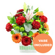 A colourful, uplifting bouquet is shown in full detail, designed by a local North Watford florist and displayed in a sleek, rectangular glass vase set against a bright white background. Wrapped neatly around the base of the vase is a soft green and white gingham ribbon, adding a friendly, homely note that feels perfectly suited to a kitchen windowsill or living room in the quiet streets off St Albans Road. The flowers themselves form a rich, layered tapestry of colour and texture. Deep red roses with gently curled, velvety petals sit alongside bright, sunlit orange gerbera daisies, each bloom defined by its dark centre and crisp, radiating petals. Between them, red-orange carnations with frilled, cushiony heads contribute a sense of intimacy and warmth, as if the bouquet has been arranged to mark a heartfelt celebration or a thoughtful thank-you. White oriental lilies rise above the main cluster; some are open, revealing soft pink streaks and prominent stamens at their centres, while others remain in smooth green buds, giving the arrangement an evolving, living quality that will continue to delight once it reaches its new home in North Watford. Pairs and clusters of lime-green pompom chrysanthemums dot the display, their tidy, globe-shaped forms offering playful contrast and a fresh, springlike brightness. Lush dark green leaves and slender sprigs of silvery eucalyptus weave throughout, adding depth, framing the brighter flowers, and suggesting a light, clean fragrance. At the bottom right of the picture, a circular orange badge overlaps the vase and reads VASE INCLUDED in bold white capital letters, clearly indicating that the glass vase forms part of this complete, ready-to-display floral gift.
