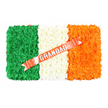An overhead photograph captures a rectangular funeral arrangement styled precisely as the Irish national flag, laid out on a plain white surface so its colours stand out clearly. The design is divided into three vertical panels of densely packed flowers, arranged so tightly that the entire piece appears like a plush cushion of petals. On the left, a deep green panel made from small, textured blossoms forms a rich, even field, symbolising growth and the Irish landscape. The central panel is composed of white flowers with soft, layered petals, giving a sense of purity, stillness, and reflection at the heart of the tribute. On the right, a panel of bright orange flowers adds a warm, glowing accent, its colour striking against both the white centre and the background. Cutting diagonally across the middle and right sections is a glossy ribbon in a coral-red shade, its surface catching light with a slight sheen. Printed boldly in silver capital letters along the ribbon is the word GRANDAD, a simple, heartfelt dedication that personalises the entire design. Delicate white pins or pearl-like studs anchor the ribbon gently to the white floral band, hinting at the careful craftsmanship behind the tribute. The mood is one of respect, remembrance, and cultural pride, blending a strong Irish identity with tender family sentiment. It is the sort of bespoke piece that might be delivered to a funeral home or cemetery in North Watford and the surrounding areas, offering a last, loving salute to a grandfather who held his Irish roots close throughout his life.