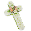 This image shows a reverent white floral cross tribute, photographed against a clear white background so that every petal and curve stands out in gentle detail. The cross is broad and substantial, its entire surface meticulously covered in tiny white button chrysanthemums. Each bloom is placed tightly beside the next, forming a thick, padded layer with no stems or gaps visible, giving the impression of a soft, cloud-like texture. The purity of the white flowers suggests peace, innocence, and spiritual comfort, the kind of arrangement North Watford families often choose for heartfelt funeral services or memorials. At the centre of the cross, where the arms meet, a graceful cluster of roses introduces a tender palette of colour. Fully open roses in soft blush pink, warm peach, and creamy ivory are gathered into a rounded focal point, petals unfolding in gentle spirals. Around them, delicate sprigs of lavender or pale purple filler flowers add a fine mist of contrasting tone. Light, feathery fern fronds extend from beneath the roses, their fresh green fronds softening the transition between the coloured cluster and the white chrysanthemum blanket. Tracing the perimeter of the cross is a narrow band of lime green ribbon, peeking from beneath the flowers to define the silhouette and lend a fresh, contemporary accent without overpowering the overall serenity. A faint shadow behind the piece emphasises its three-dimensional depth and sturdy construction. The design reads as a thoughtful, handcrafted sympathy tribute, suitable for delivery to chapels, crematoria, or gravesides across North Watford, expressing faith, remembrance, and the enduring bond between the departed and those who mourn them.