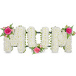 This photograph shows a traditional MUM funeral tribute presented on a clean white background, designed with the quiet elegance that many families in North Watford look for when saying goodbye. The three bold letters are shaped from a sturdy frame but appear entirely covered in flowers, thanks to the dense layer of white spray chrysanthemums packed closely together. Their small, rounded petals form a soft, even surface, giving the impression of fluffy white cushions laid side by side. At the base of each letter, a narrow band of dark green ribbon or foliage reveals the structure beneath and gently outlines the shapes, offering contrast without overwhelming the purity of the white blooms. To break the expanse of white and add emotional warmth, three coordinated flower sprays are placed with intention. The first sits at the top left of the opening M, where a striking fuchsia rose blooms in full, surrounded by lighter pink spray roses and delicate buds. Fine tendrils of fern leaf curl around the petals, bringing a touch of woodland greenery. A second cluster nestles into the lower curve of the U, and the final one rests at the upper right of the closing M, echoing the same colours and textures to create a graceful flow across the tribute. Crafted in a style often requested from local florists for funeral services and memorials, this MUM arrangement speaks through its colours and shapes of love, gratitude, and the gentle remembrance of a mother's presence.