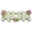 A deeply felt funeral tribute spells the word MOM in bold, three-dimensional letters entirely covered in snowy-white spray chrysanthemums, their tiny petals packed so closely they form a soft, cloud-like surface that reads as purity and calm. The left M carries a graceful cluster of pastel pink and lavender roses and buds on its upper outer curve, the central O is gently cradled by a smaller grouping at its base, and the right M mirrors the left with a matching spray of lilac roses and pale pinks on its upper right arm. Wisps of fern fronds and bright green foliage peek through and around the clusters, offering a fresh, verdant contrast to the luminous white and lending depth and gentle movement to the piece. A darker green structural band - ribbon-wrapped or moss-covered - runs along the base and behind the letters, visible as a subtle line that keeps each letter firm and unified without distracting from the blossoms. The overall effect, captured in soft daytime light, is one of hushed reverence: the white chrysanthemums suggest peace and remembrance, while the lavender and blush roses lend tenderness and affection. As a local florist might explain before placing it by a chapel or graveside, this arrangement is shaped to be seen clearly from the front of a service, to sit respectfully by a coffin or on an easel at a wake, and to speak a quiet, consoling message. The design feels handcrafted and steady, the textures smelling faintly of fresh green stems and garden roses - a composed, intimate tribute intended to honour a mother with dignity and love across North Watford and nearby communities.