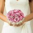 Held with loving hands by a North Watford bride, this bridal bouquet is a masterclass in delicate contrasts and joyful celebration. The roses captivate instantly: their petals unfurl in soft spirals that transition seamlessly from a pale, blush pink at each centre to a vivid, magenta rim, mimicking the gentle sunrise one might catch over North Watford's gardens. Misty sprays of fine white baby's breath drift among the blooms, their airy texture lending a veil-like softness and infusing the scene with innocence and romance. Close up, you sense the silkiness of the rose petals juxtaposed against the feathery lightness of the gypsophila, all highlighted by natural daylight tumbling over the intricate floral lace of the bride's gown. The warmth and anticipation in the bride's gently curved hands - nails manicured in understated hues - tell of both calm and bubbling excitement. A flowing sash ties on one side, emblematic of movement and grace. The serene, blurred neutral background focuses all attention on the blossoms' colours and textures, evoking North Watford's local charm and the excitement of celebrations shared with friends and family in familiar places. This bouquet is more than a bridal accessory; it's an expression of hope, artistry, and the promise of happiness, as crafted by North Watford's most passionate florists.