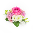 Set against a pristine white backdrop, this compact corsage reads like a whispered promise-an intimate study in pinks, creams, and verdant green. At its centre a lush bubblegum-pink rose unfurls in many velvety layers, its inner petals still tightly curled while outer petals open with soft resilience. Nestled around it are clustered hydrangea florets in pale pink and a cool lavender-tinged blush, their tiny rounded petals creating a billowy, romantic cushion. Interspersed among the pinks are a few small trumpet-shaped white blooms-suggestive of miniature amaryllis or lily forms-with a faint green wash at their throats that brightens the composition. Deep, glossy green leaves fan beneath the flowers, broad and anchoring, offering a cool, textured contrast to the rose's plush surface. Along the sides, slender fresh green buds tipped with a hint of yellow introduce a forward, hopeful movement, as if the piece is still waking up toward full bloom. At the lower right, a delicate spray of pearlescent beads clusters like heirloom jewellery, catching the light and lending a refined, bridal-ready accent. The lighting is soft and natural, bringing out the rose's satin sheen and the hydrangea's whispery translucence while suggesting a faint, clean garden scent-a gentle mix of rose sweetness and green freshness. This arrangement has the quiet elegance of a wedding corsage or prom accessory and the careful craftsmanship of a neighbourhood florist preparing final touches for milestone celebrations in and around North Watford. It reads as both modern and timeless: tender, wearable, and quietly celebratory.