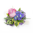 Pinned against a clean white backdrop, this compact corsage reads like a small, personal poem: a single, regal rose opens at its center in a pale lavender-pink that deepens to a lively fuchsia at the outermost petals, its velvety curve the quiet focal point. To the right, a tight cluster of indigo-purple florets - recalling miniature hydrangea or delphinium heads - catches the eye with tiny bright-blue and lime-yellow-green centers that glint like garden jewels. Surrounding those blooms, variegated ivy leaves lend structure and contrast: deep emerald interiors rimmed in a warm golden-yellow, their glossy texture framing the flowers with classic drama. Cooler, silvery-green foliage-suggestive of lavender leaves-softens the composition with muted, dusty tones, while a long, striped green-and-cream blade of grass is artfully curled to introduce sculptural movement. Airy, feathery sprigs of light-green asparagus fern are threaded throughout, adding breath and a soft, filigree texture that lifts the arrangement off the surface. Beneath it all a dark purple, web-like mesh peeks out, its intricate pattern adding depth and a subtle, modern shimmer when the light catches it. A short strand of lustrous white pearls sits at the lower right edge, implying a wristlet or decorative flourish that anchors the piece in tradition. The whole accessory, imagined in soft morning light, feels both romantic and contemporary-perfect to pin at a Cassiobury Park wedding, wear to a North Watford celebration, or tuck into a prom outfit for a moment that will be remembered by touch as well as sight.