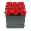 A luxurious square arrangement of red roses is captured from eye level, as though set on a table in a stylish North Watford home, ready to be handed to someone special. Twelve rich crimson roses are tightly packed in a precise 3x4 grid, their open blooms creating a near-seamless surface of velvety petals. Each rose appears remarkably consistent in size and shape, the petals curling inward in intricate, layered whorls that signal premium preserved roses, chosen to retain their beauty long after the day of delivery. Their colour is a deep ruby red, with subtle shifts in tone that emerge where the soft, diffused light kisses the outer petals, hinting at texture and depth even without touch. These blooms are nestled in a sleek, matte black square box with sharp, defined corners, exuding understated luxury. A narrow white stripe encircles the lower edge of the box like a minimalist border, adding just enough contrast to emphasise the modern design without drawing attention away from the roses. The entire composition sits against a crisp white backdrop, completely uncluttered, allowing the bold red and black palette to stand out clearly. Soft, even lighting eliminates harsh reflections, instead creating gentle shadows that define the curves of the roses and the geometry of the box. The overall impression is of a contemporary, romantic gift-perfect for same-day delivery across North Watford, whether to mark a proposal in a cosy flat near Garston, to celebrate an anniversary after a walk around local green spaces, or to serve as an elegant, long-lasting centrepiece in a minimalist living room.
